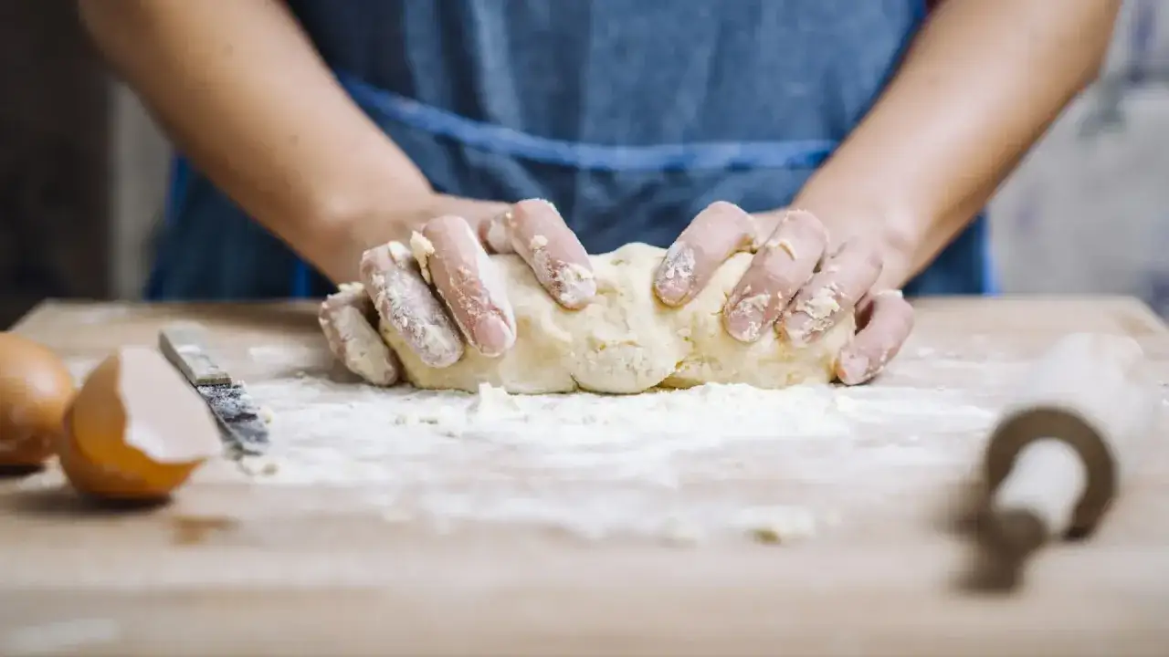 Manos amasando masa para pasta fresca sobre una tabla de madera. Huevos y rodillo cerca.
