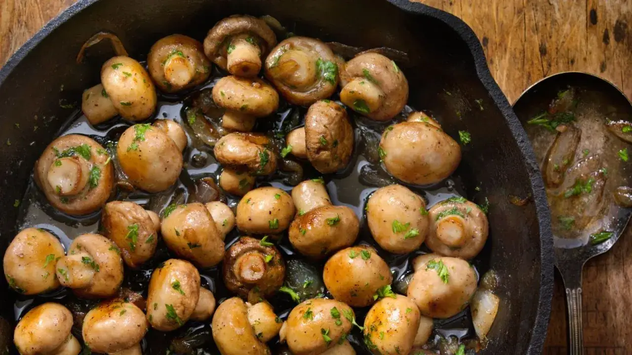 Champiñones salteados en sartén de hierro fundido, listos para ser parte de deliciosas recetas con champiñones.