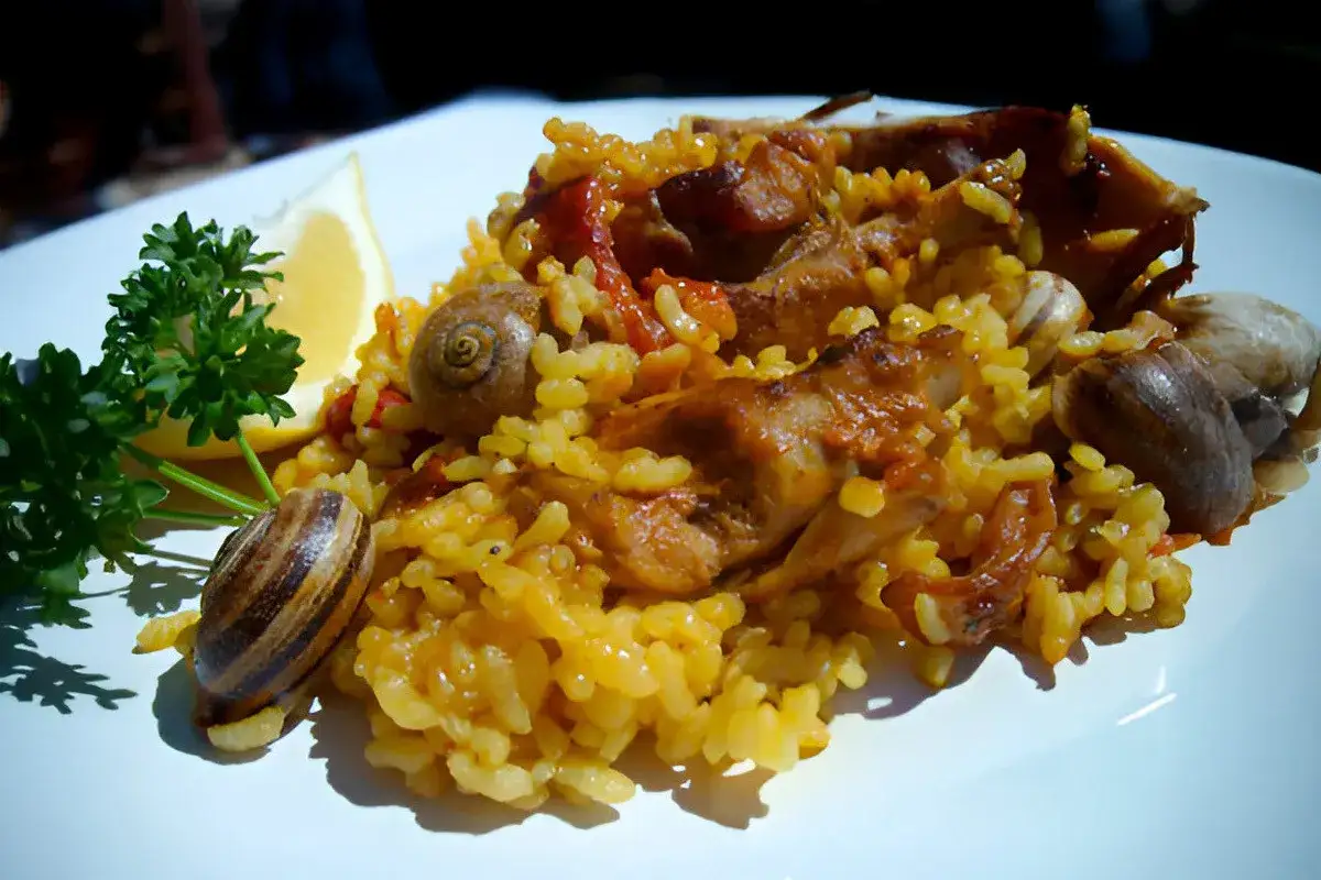Arroz con conejo y caracoles, servido con perejil y limón. Un plato tradicional y sabroso.
