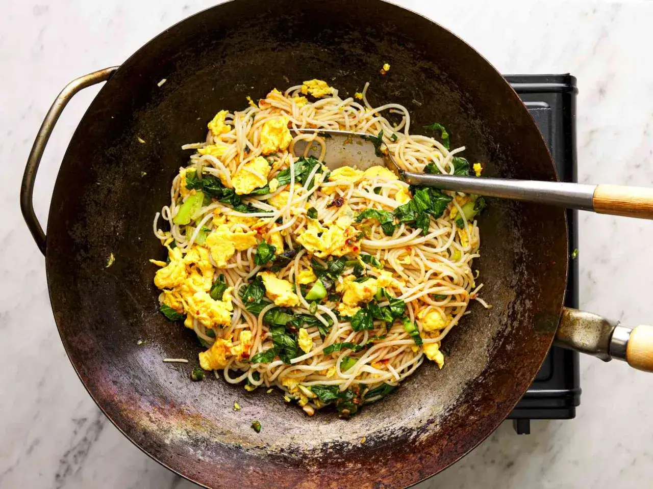 Fideos de arroz salteados con huevo revuelto y verduras verdes en un wok.