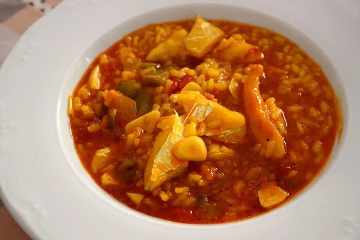 Un plato de arroz con bacalao, lleno de trozos de pescado blanco tierno y verduras en una salsa rojiza.