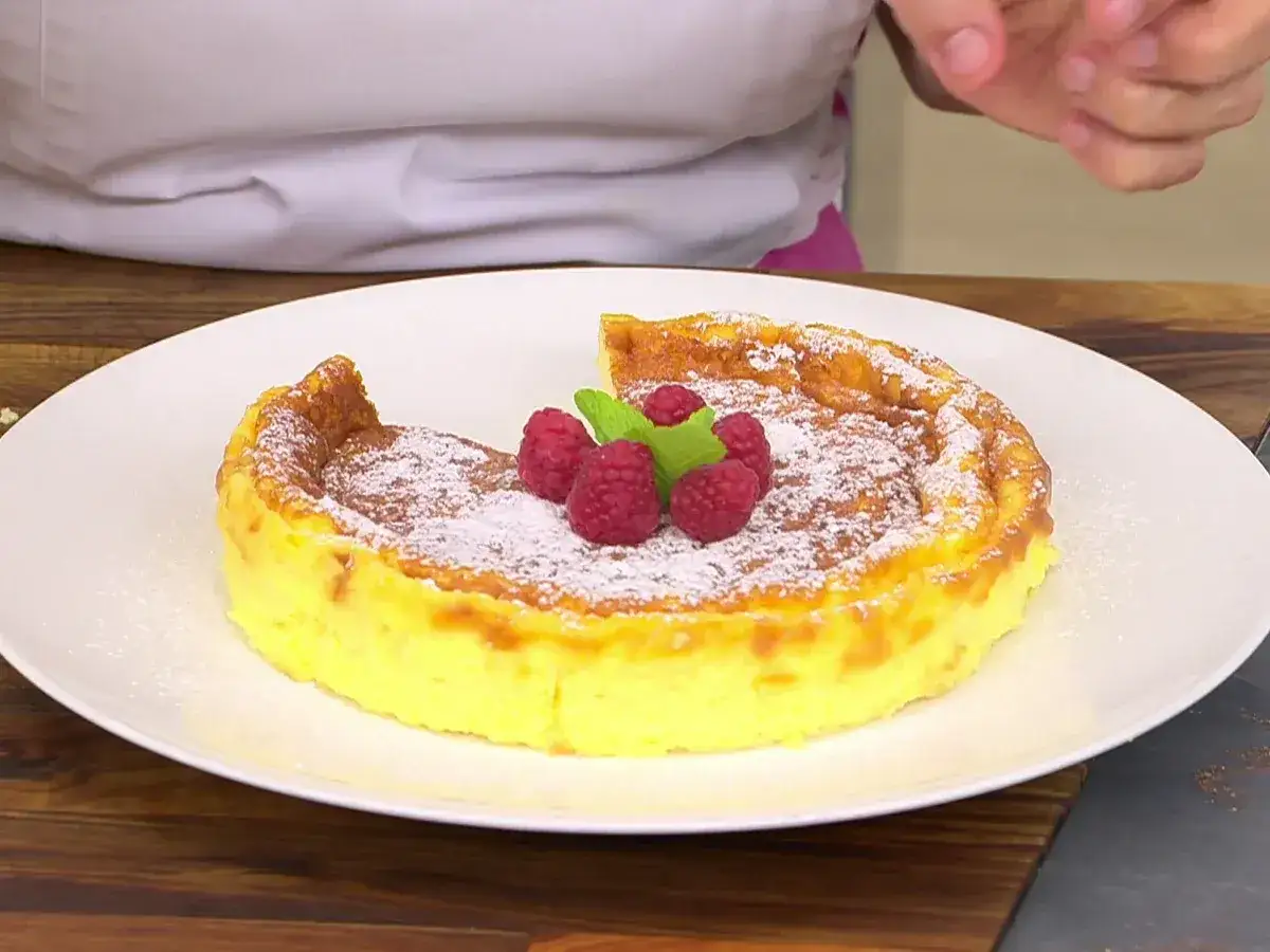Tarta de queso Eva Arguiñano, dorada y esponjosa, espolvoreada con azúcar glas y decorada con frambuesas y menta.
