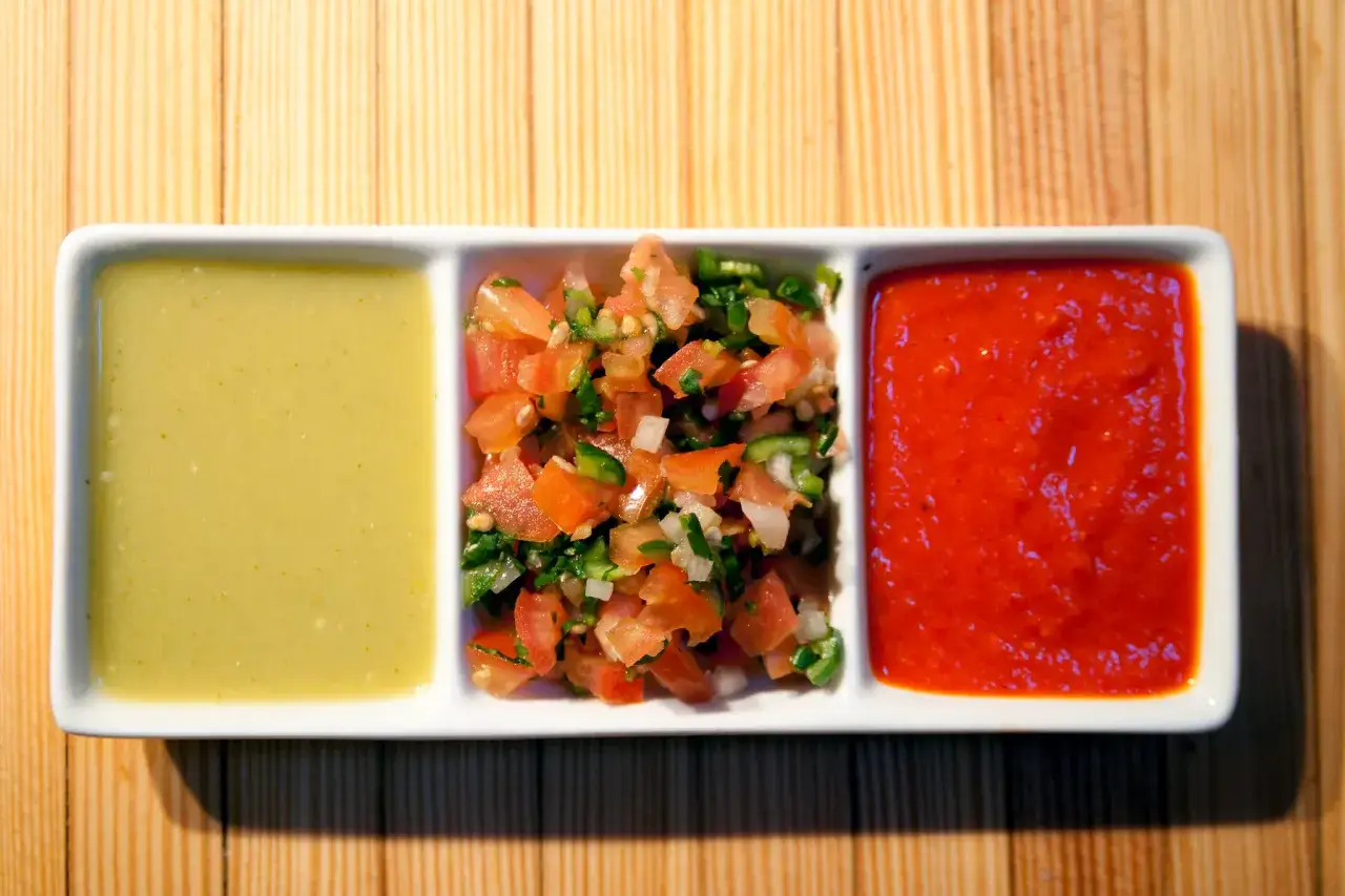 Tres salsas en un plato blanco: una verde cremosa, una pico de gallo fresca y una roja vibrante, perfecta para acompañar tu salsa ranchera.