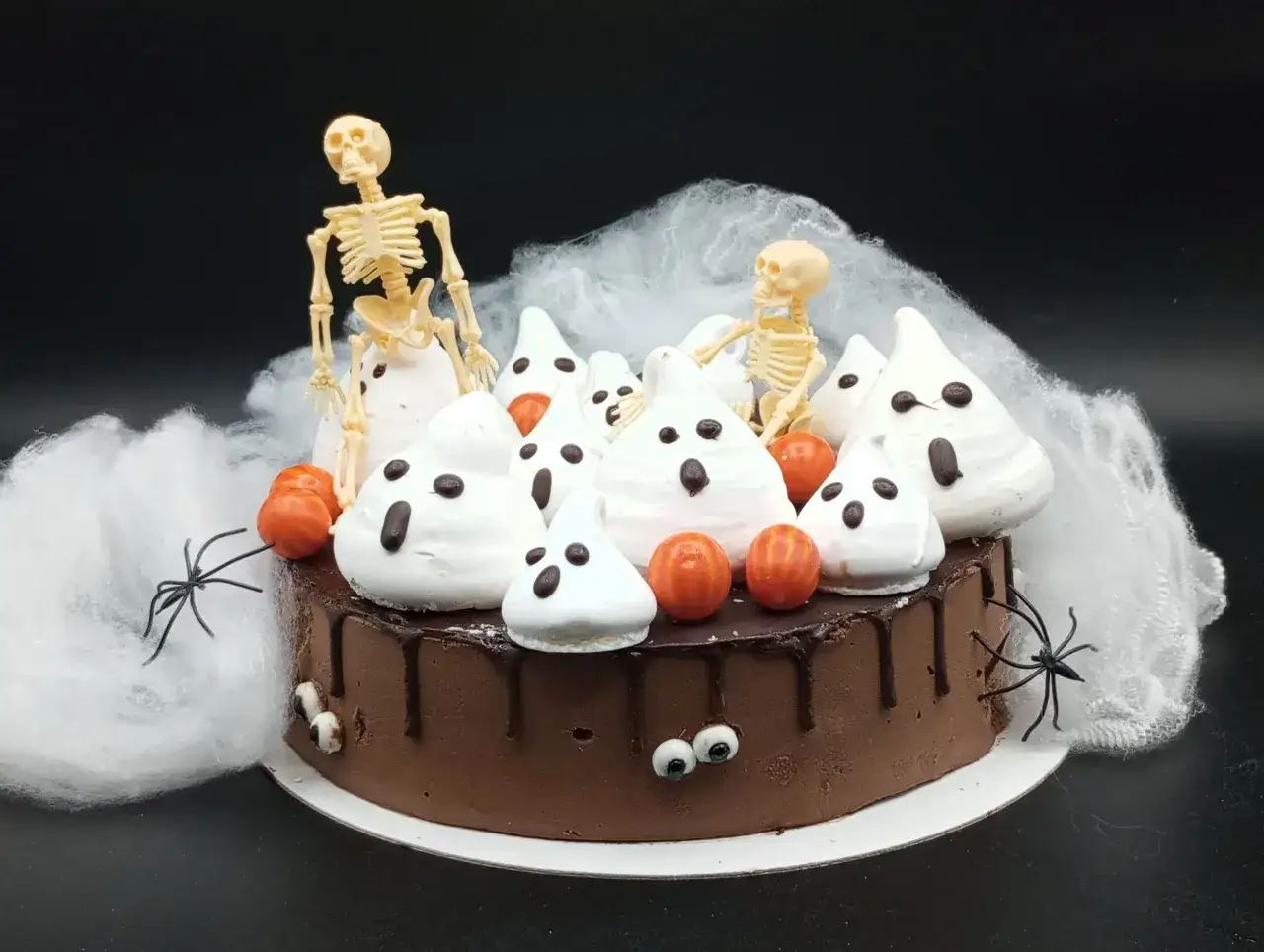 Tartas de Halloween originales: un pastel de chocolate cubierto de fantasmas de merengue, calabazas y esqueletos, rodeado de telarañas y arañas.