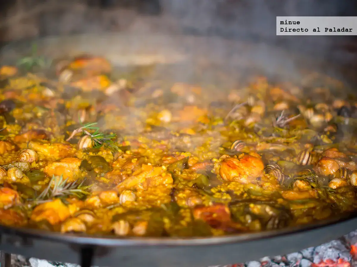 Una humeante paella valenciana que lleva caracoles, pollo y verduras, cocinándose a fuego vivo.