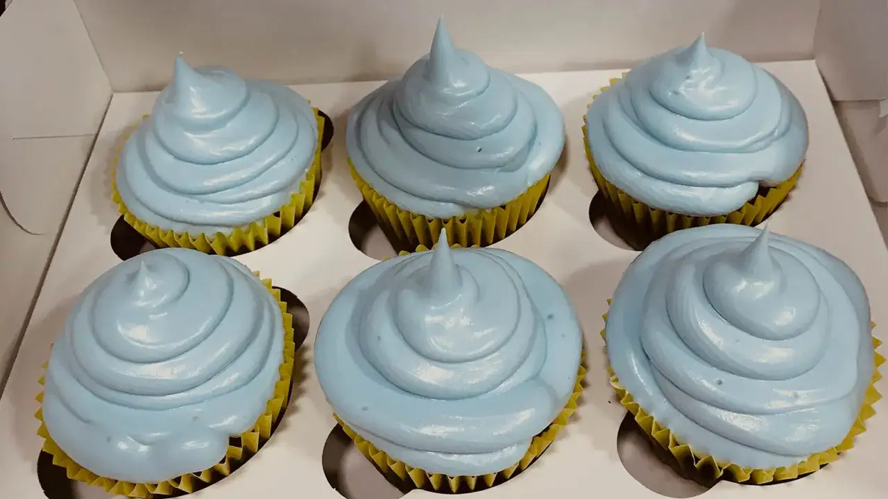 Seis cupcakes con glaseado de merengue italiano azul p&aacute;lido, en sus envoltorios amarillos, listos para ser disfrutados.
