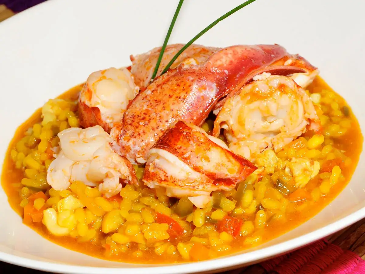 Delicioso arroz con bogavante, con trozos de bogavante jugoso sobre un arroz amarillo con verduras.