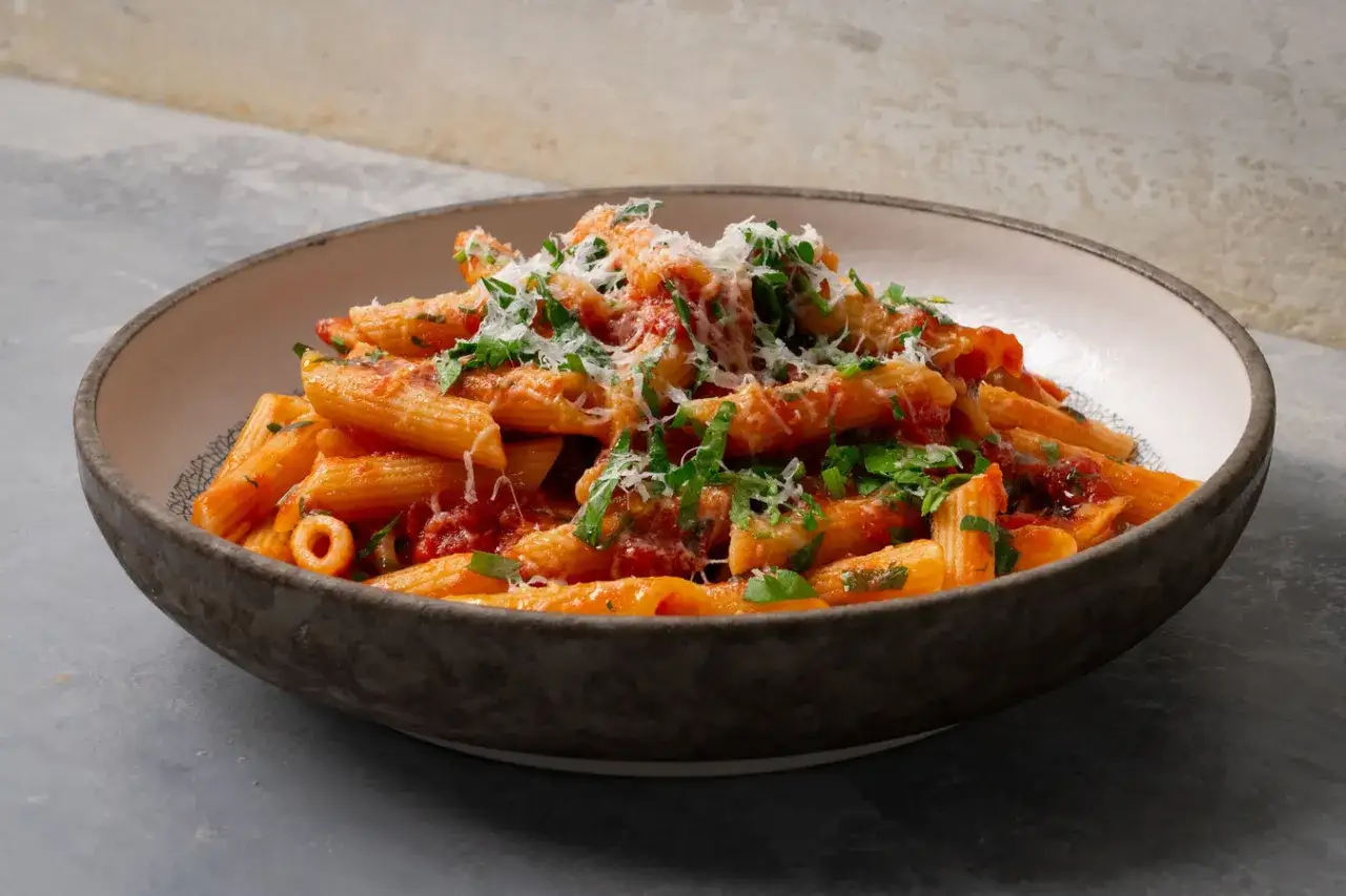 Penne rigate con una vibrante salsa arrabiata, cubiertas con queso rallado y perejil fresco.