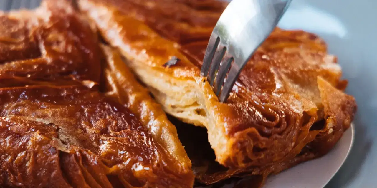 Un tenedor se hunde en un crujiente y caramelizado kouign amann, revelando sus capas hojaldradas.