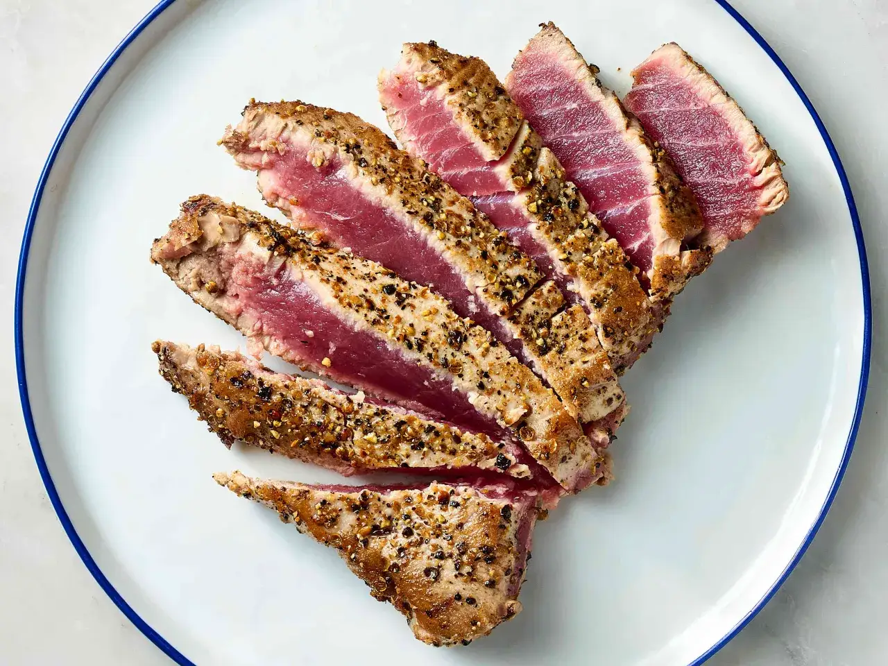 Rodajas de at&uacute;n a la plancha, con un exterior dorado y un interior rosado, cubiertas de especias y pimienta negra.