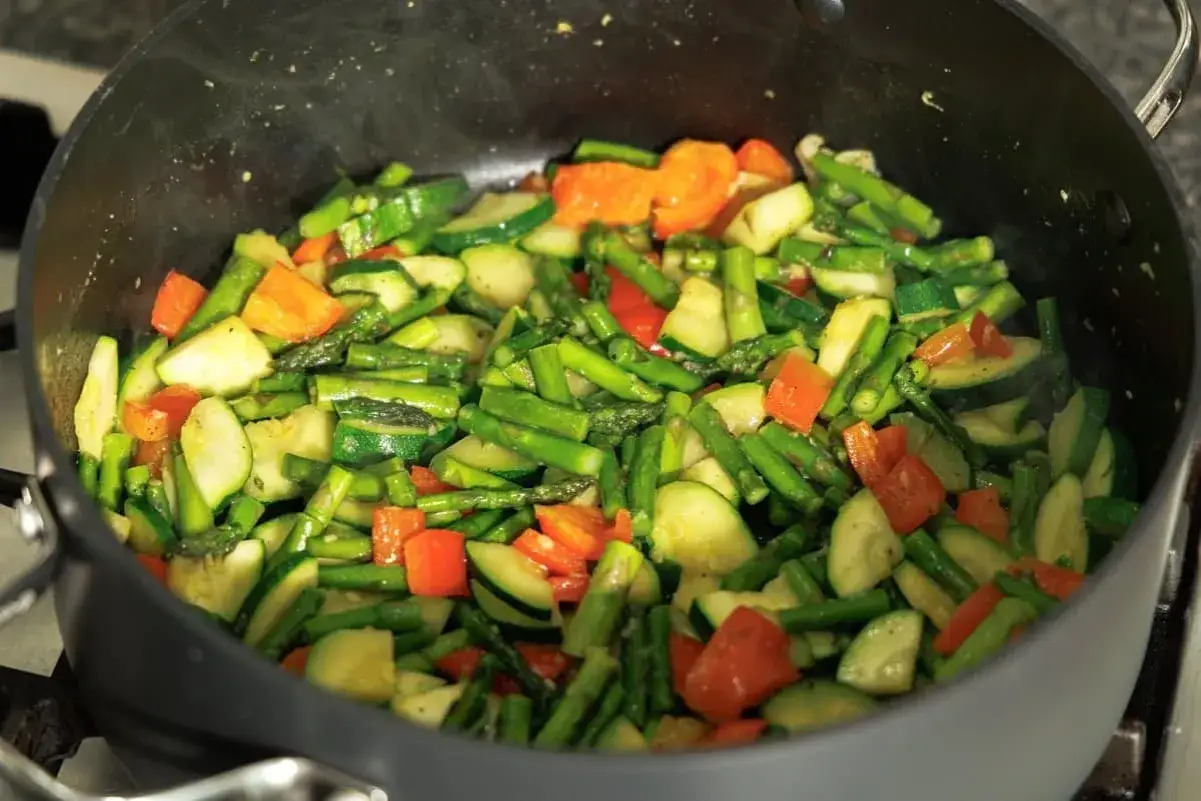 Verduras salteadas en una sart&eacute;n: esp&aacute;rragos, calabac&iacute;n y pimientos rojos, listas para mezclar con pasta.