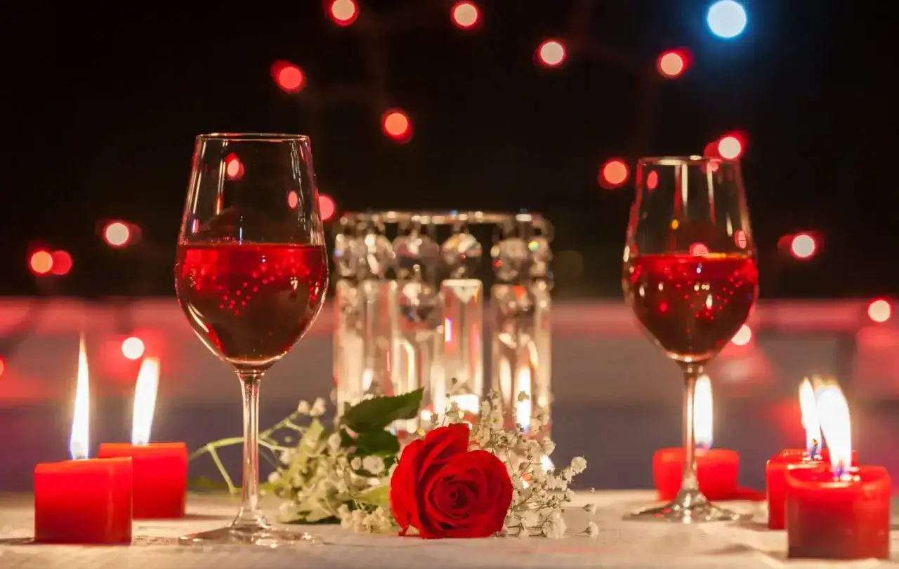 Dos copas de vino tinto, una rosa roja y velas rojas crean una velada romántica en casa.