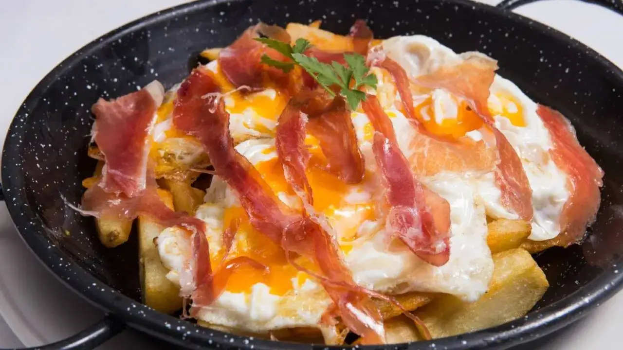 Huevos rotos con patatas fritas y jamón serrano, un plato delicioso y contundente.