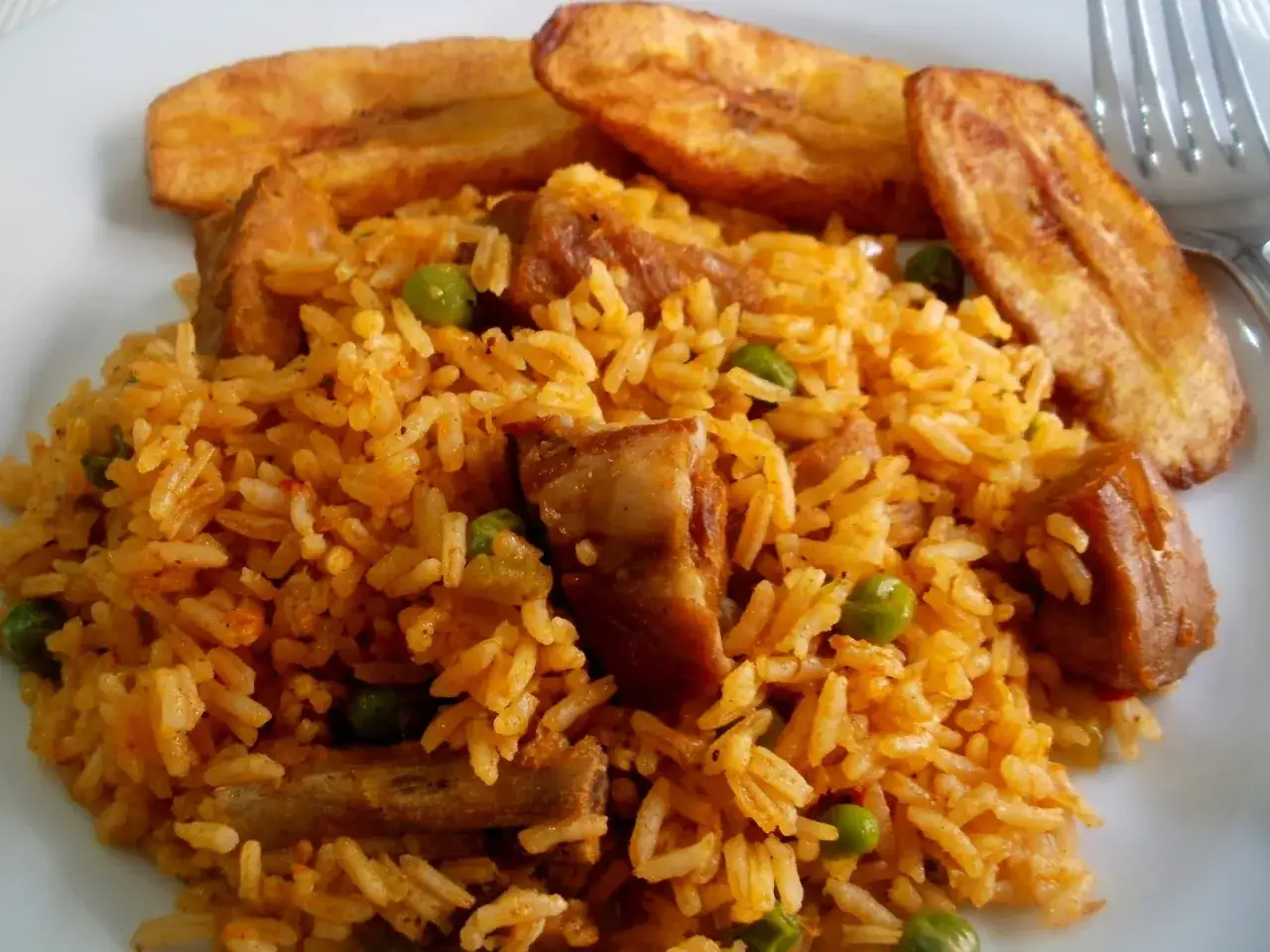 Delicioso arroz con costillas, guisantes y plátanos fritos en un plato blanco.