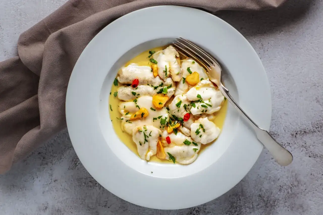 Bacalao al pil pil, un plato tradicional con trozos de pescado blanco en una salsa dorada, adornado con perejil picado y guindilla.