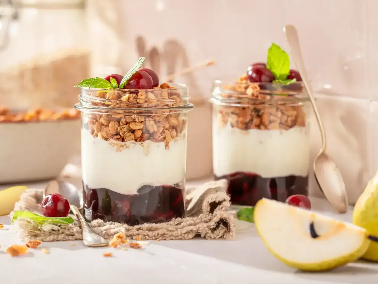 Dos vasos con postres saludables: yogur, granola, cerezas y menta.
