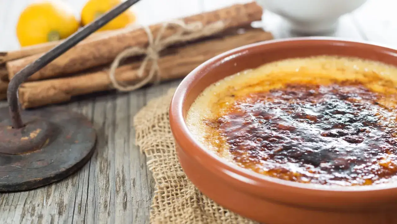 Crema catalana con una capa crujiente de caramelo, lista para ser disfrutada. Al fondo, limones y canela en rama.