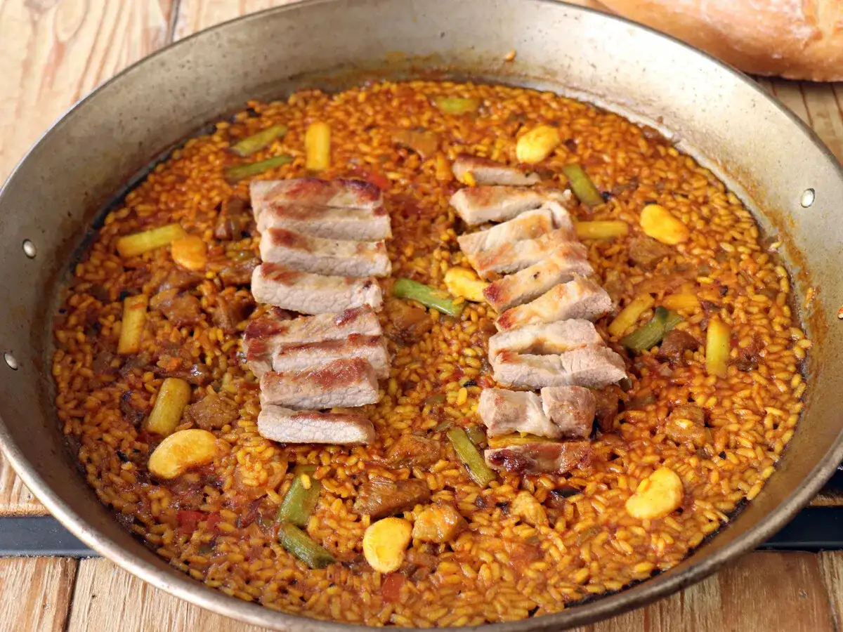 Paella de arroz con secreto ib&eacute;rico, jugosas tiras de cerdo y verduras en una paellera.
