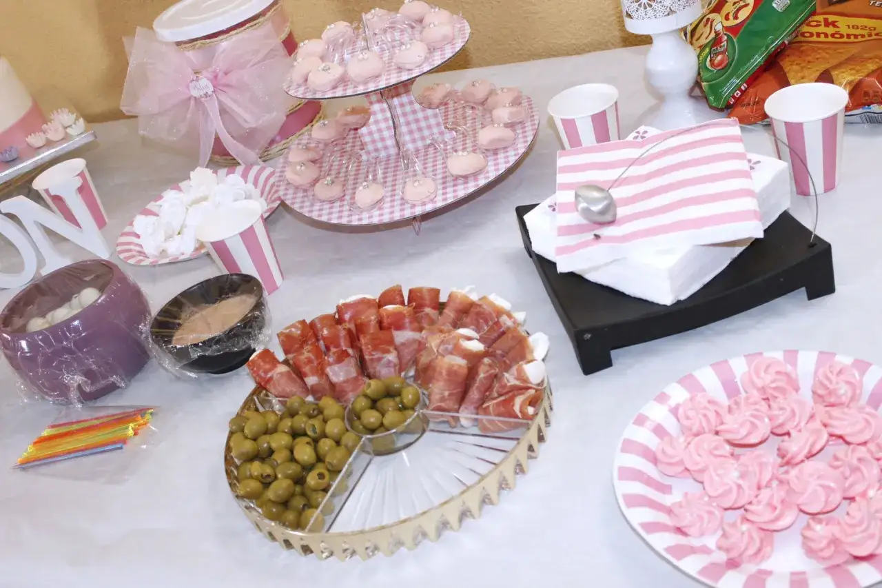 Deliciosa comida para baby shower: jam&oacute;n serrano, aceitunas, merengues rosas y dulces en bandejas.