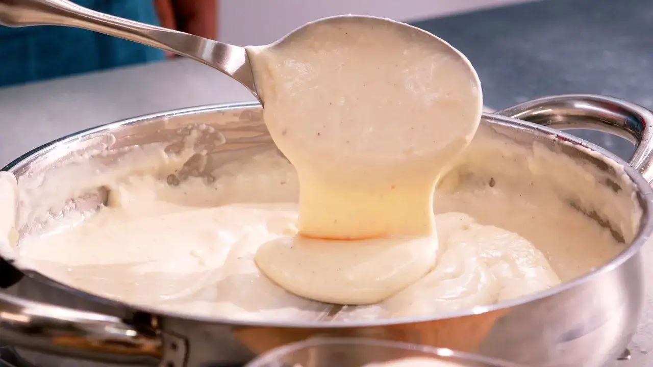 Cremosa bechamel receta vertiéndose de una cuchara a una olla.