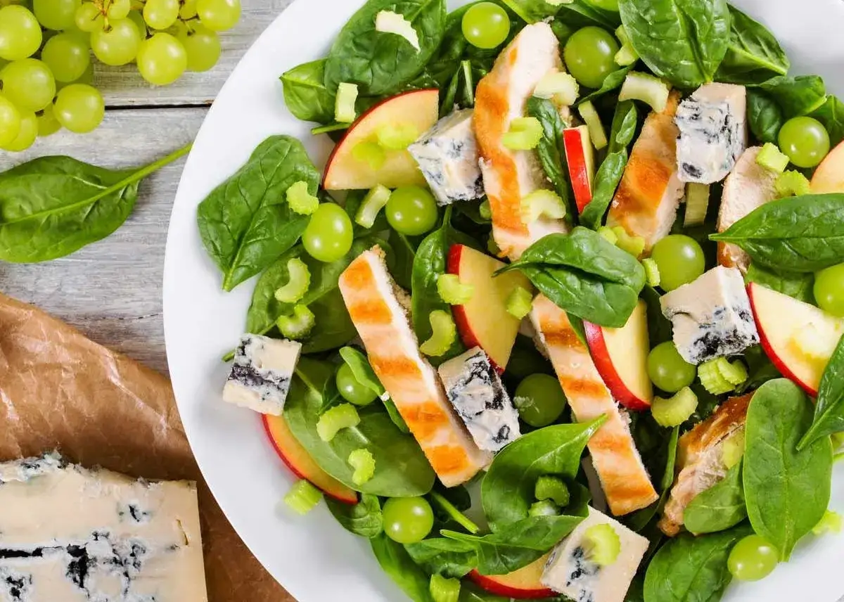 Ensalada de pollo con espinacas, uvas verdes, trozos de manzana roja, apio y queso azul.