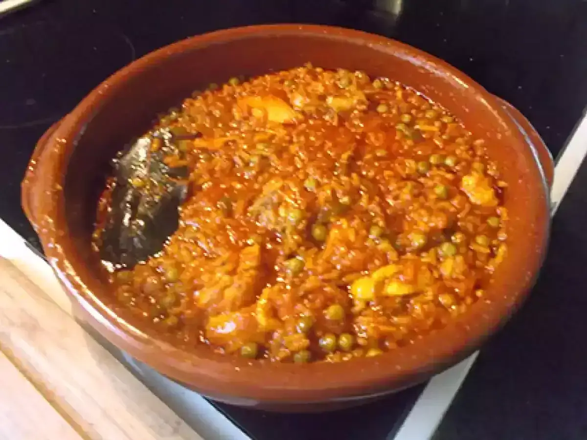 Un delicioso arroz caldoso con pollo, guisantes y un sofrito rojizo, servido en una cazuela de barro.