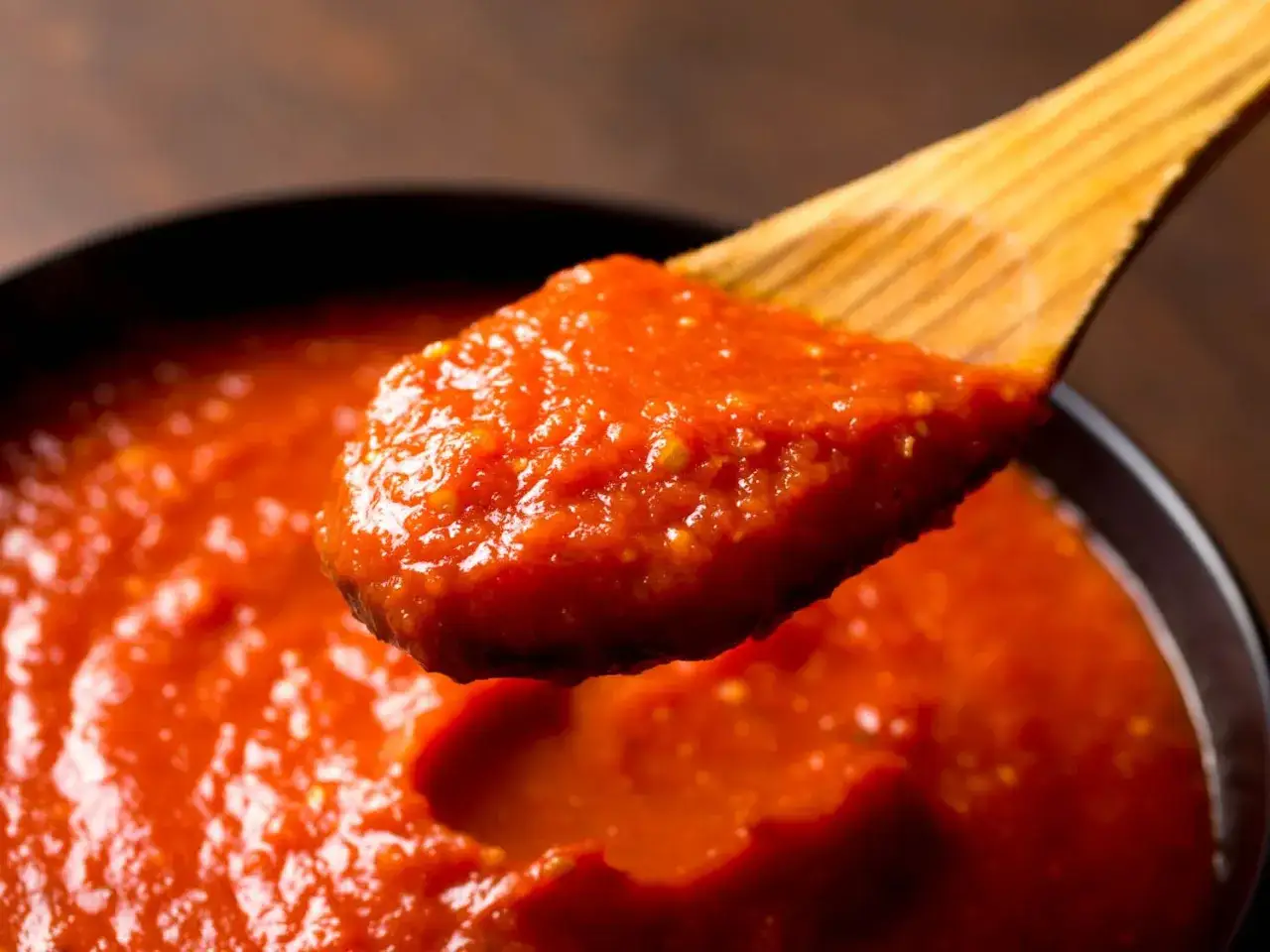 Cuchara de madera con salsa napolitana casera, lista para aderezar pasta o pizza.