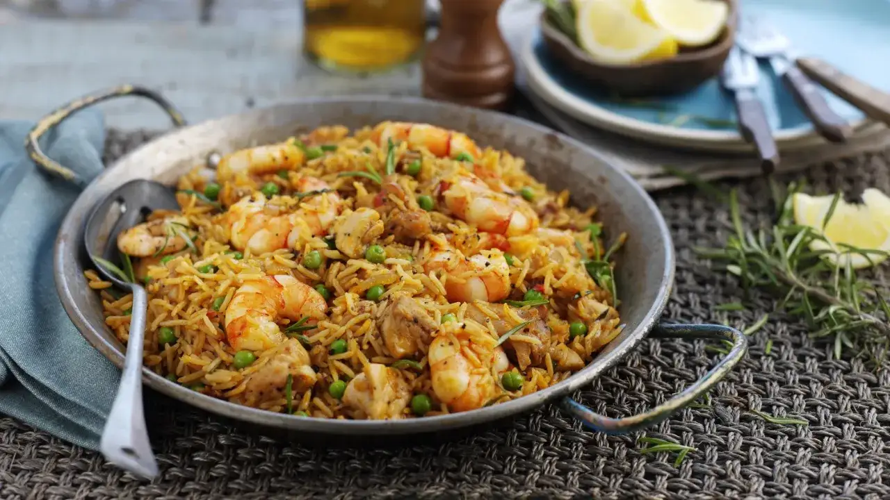 Paella mixta humeante en su paellera, con gambas, pollo y guisantes, lista para ser disfrutada.