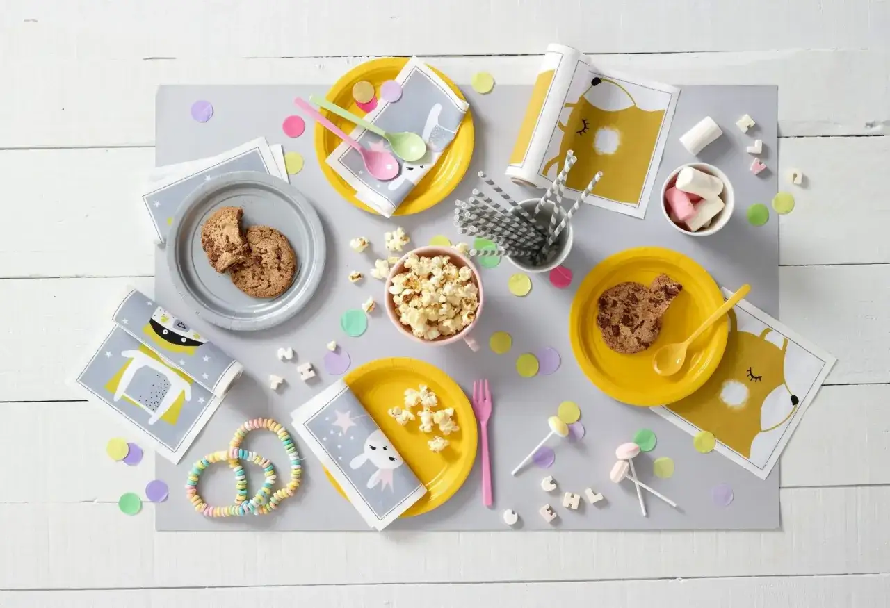 Mesa lista para un picoteo de cumpleaños infantil: galletas, palomitas, caramelos y servilletas con divertidos diseños de animales.