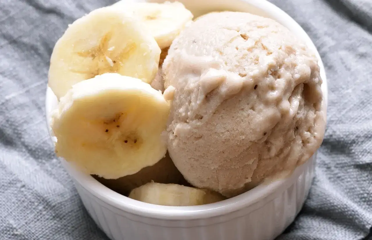 Delicioso helado de pl&aacute;tano cremoso servido en un cuenco blanco, adornado con rodajas frescas de pl&aacute;tano.