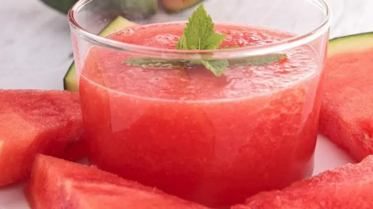 Refrescante gazpacho de sandía en vaso, adornado con menta, rodeado de trozos de sandía jugosa.