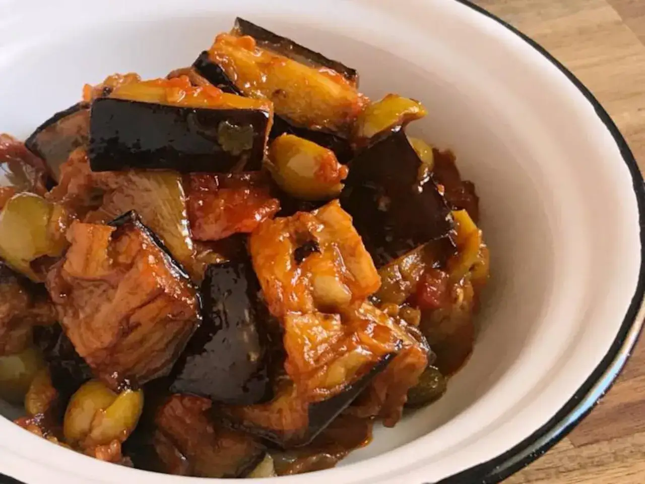 Caponata siciliana, un plato vibrante con berenjenas, aceitunas y tomate, servido en un cuenco blanco.