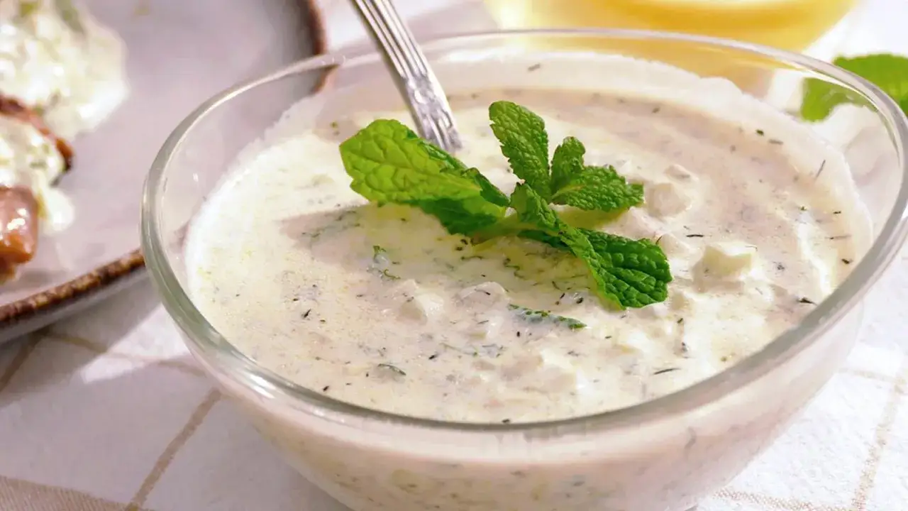 Crema de yogur con pepino y menta, la deliciosa salsa tzatziki, servida en un cuenco de cristal con una ramita de menta fresca.